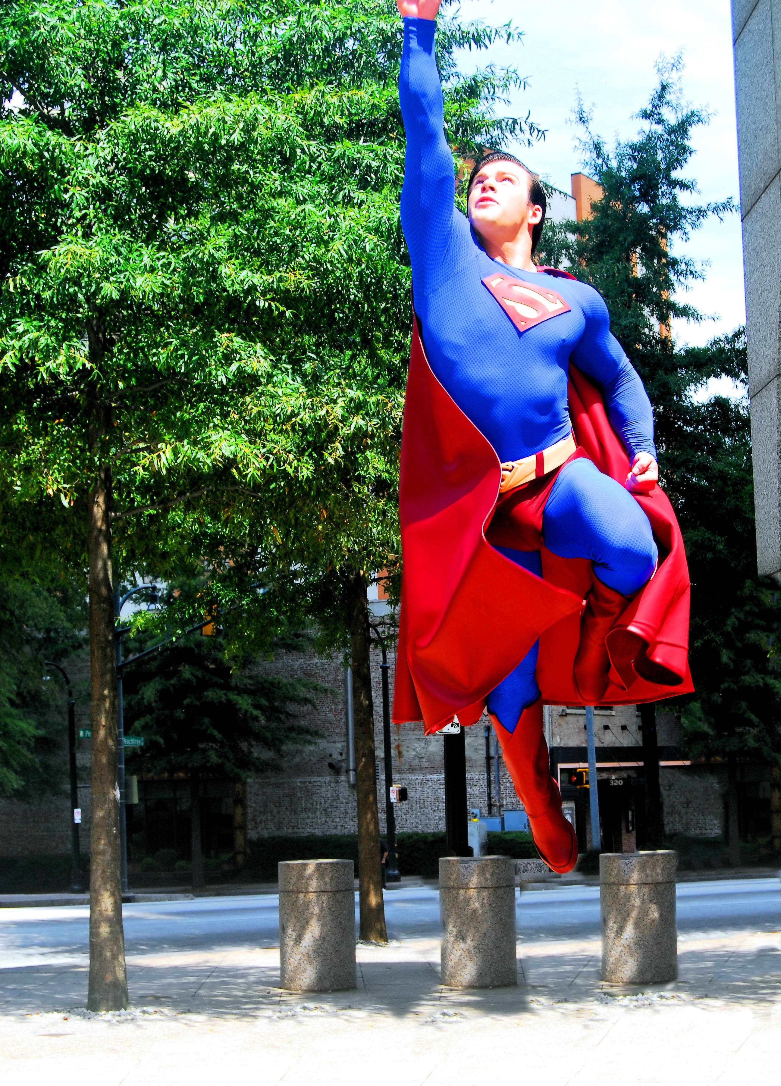 A Superman cosplayer in a blue suit and red cape leaping upward with one arm raised