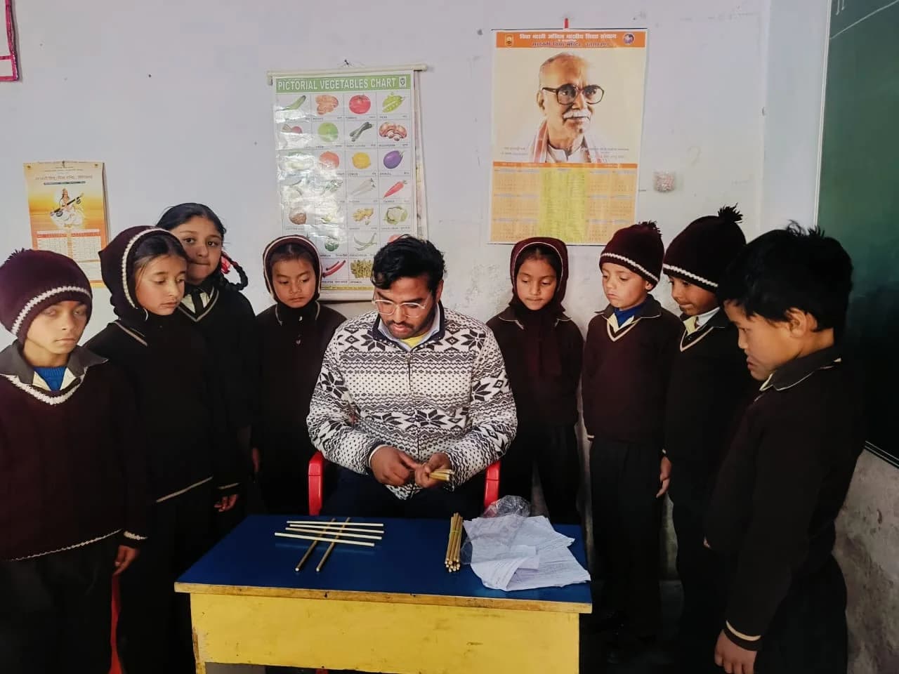 A student volunteer demonstrating an activity with wooden sticks to schoolchildren in a classroom