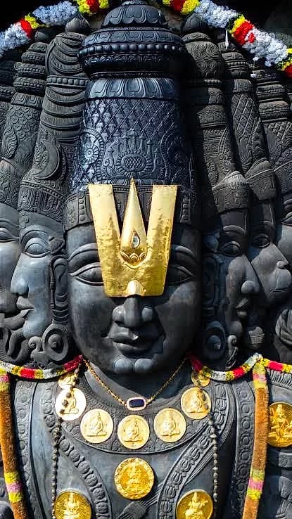 A close-up of a crowned, multi-faced stone temple mūrti garlanded for worship