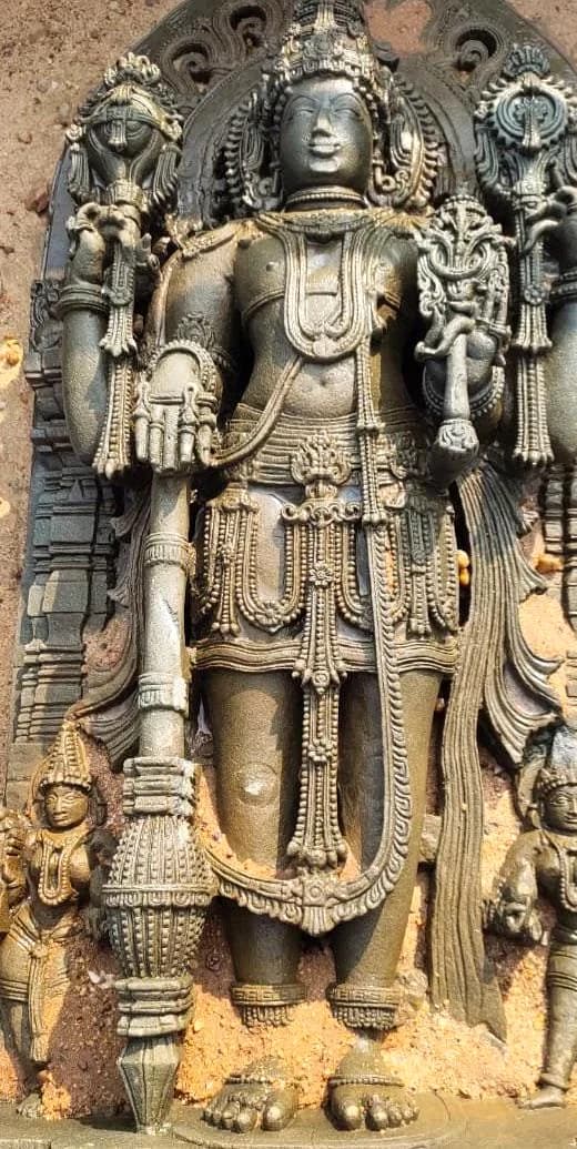A traditional South Indian temple relief sculpture of Vishnu holding the conch, discus, mace and lotus, flanked by two smaller attendant figures
